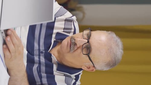 Vertical video of Home office worker old man reading bad news and feeling frustrated.