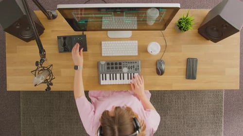 Overhead View Of Female Musician At Workstation With Keyboard And Microphone In Studio