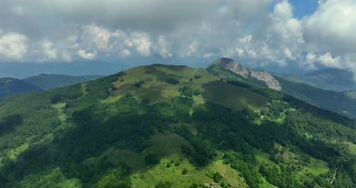 Flight over green mountain peaks. A beautiful sunny summer day at high altitude with thick clouds an