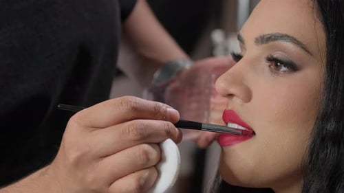 The Makeup Artist Paints the Model's Lips with Bright Lipstick