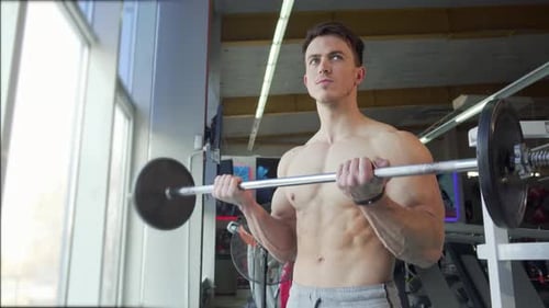 Ripped Shirtless Young Bodybuilder Lifting Barbell Showcasing Biceps Strength