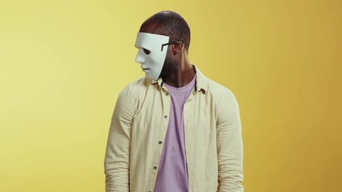 Ein Mann mit weißer Maske steht vor gelbem Hintergrund