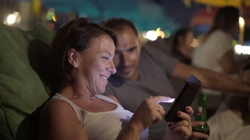 Young, Happy Couple Browsing Internet on Smartphone Sitting in Cafe at Night Adult