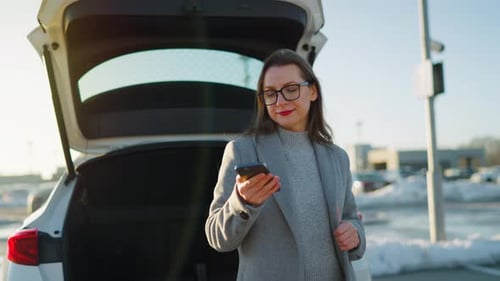 Woman Using Phone Near Open Car Trunk