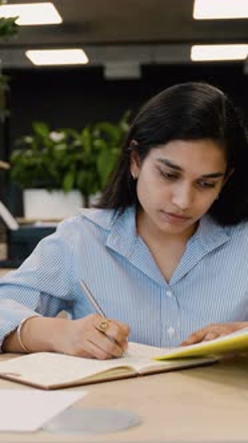 Young Woman Writes in Notebook at Bright Office Desk