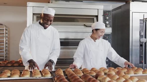 Portrait of happy diverse bakers working in bakery kitchen with fresh rolls in slow motion