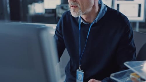 Hübscher Ingenieur mittleren Alters mit Brille arbeitet am PC. Im Hintergrund High Te