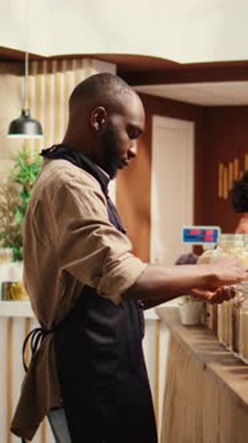 Vertical Video Merchant with Apron Placing Bulk Items on Shelves at Eco Store