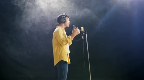 Side View Of Young Asian Boy With Headphone Singing On The White Smoke Black Background