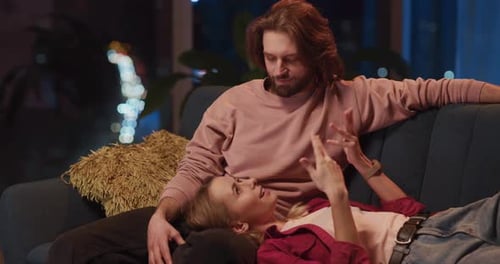 Couple of Caucasian Bearded Boyfriend and Pretty Girlfriend Sitting on Cozy Sofa and Communicating