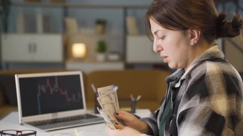 Woman Counting Money at Desk with Stock Graph