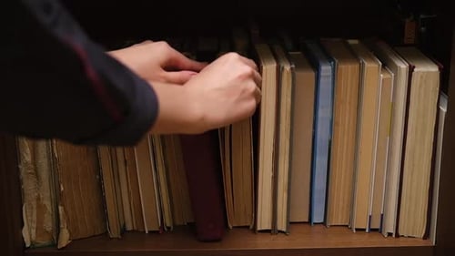 Una estantería con libros antiguos en el armario Una mano de mujer recorre los lomos de los libros en busca de