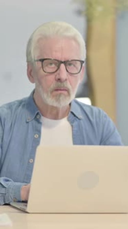 Senior Man Works on Laptop at Table Indoors