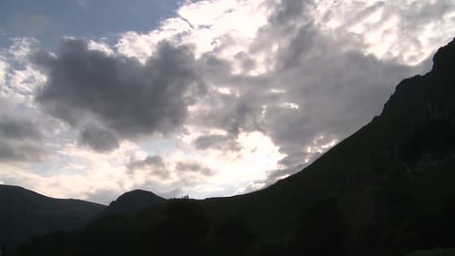 Time lapse over the silhouette of mountains with dramatic clouds passing and the sun showing up at t