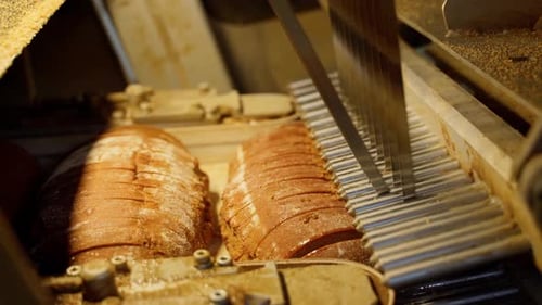 Bread cutting mechanism on a conveyor line in a factory indoors. Close-up