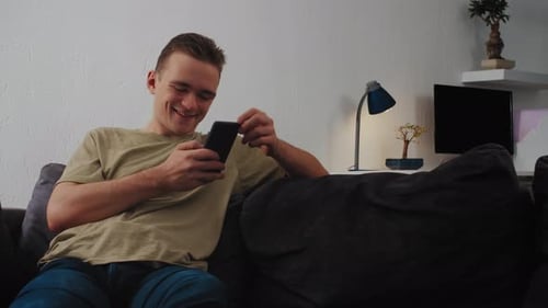 Young Man Relaxes on Couch Using Smartphone