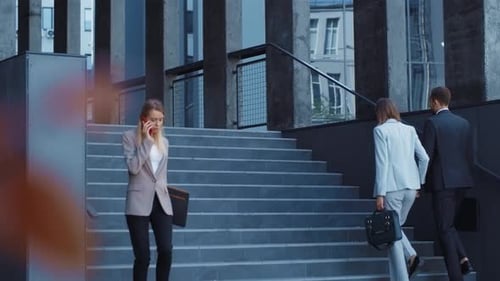 A Professional Businesswoman is Engaged in a Phone Conversation Outside a Modern Building