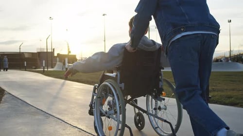 Dad Accompanies His Son with Special Needs on Stroll in Wheelchair to City Park Where They Have