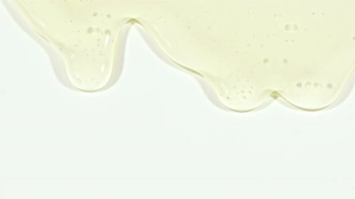 Yellow Transparent Cosmetic Gel Fluid With Molecule Bubbles Flowing On The Plain White Surface
