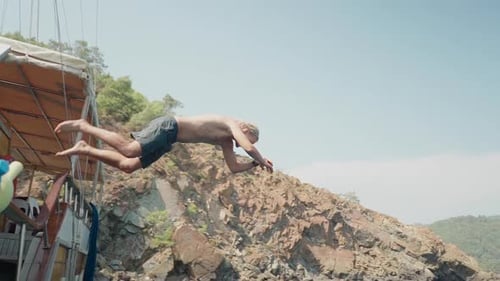 Slo Mo: Young man swan dives from sailboat into turquoise sea water