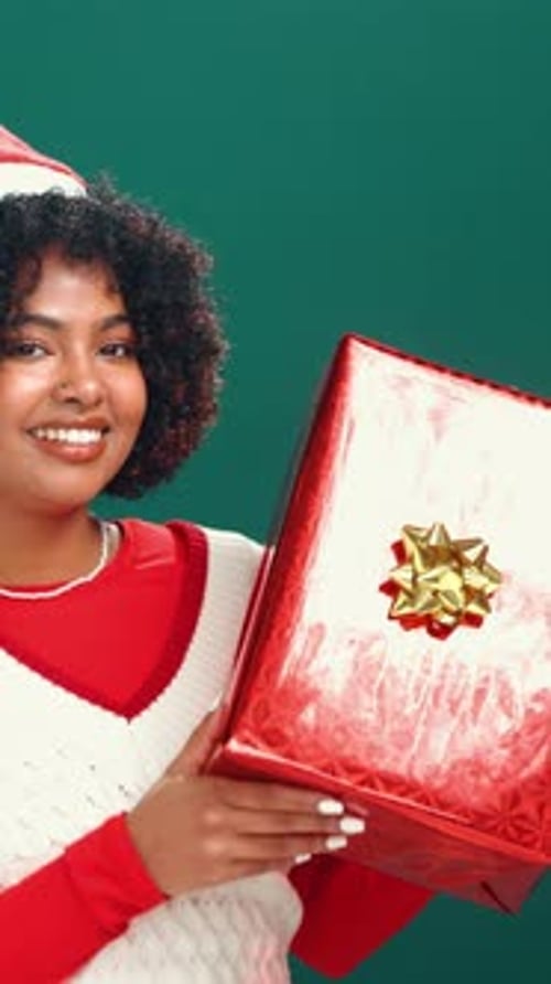 Woman, face and Christmas gift in studio, shake or listen for festive holiday on green background