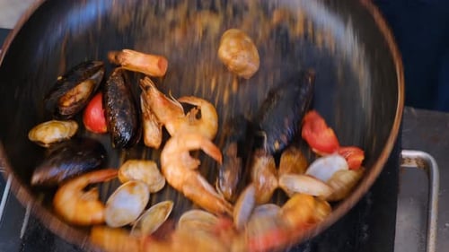 Vue de dessus d'un chef cuisinant des fruits de mer dans une poêle en mélangeant des huîtres, des palourdes et des crevettes avec des mouvements brusques