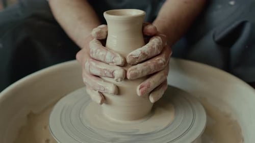 Artisan inconnu faisant glisser ses mains sur un vase en argile en le façonnant sur un tour de potier