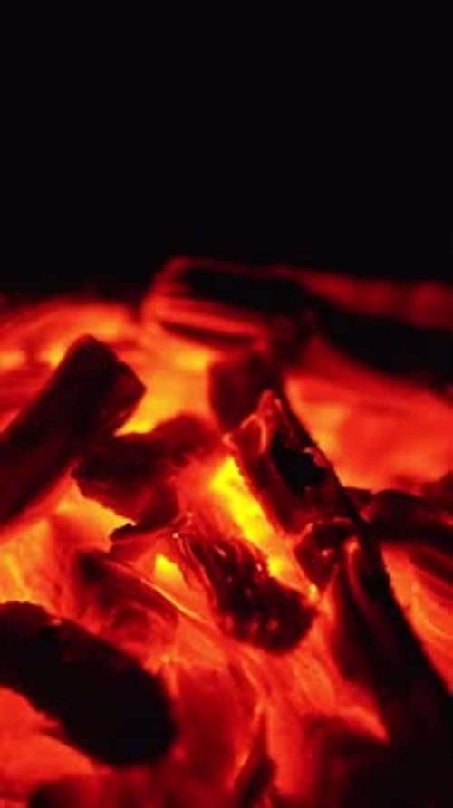 A pile of smoldering embers close up. Little tongues of flame and sparks appear on the coals.