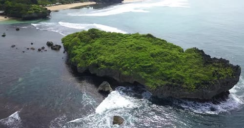 Aerial view of huge coral rock overgrown with grass vegetation on the beach that crushing by the wav