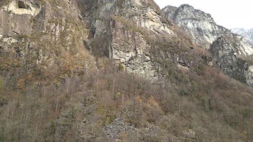 Grey rock formations are covered with leafless trees, rocky slopes are surrounded by yellow grass, C