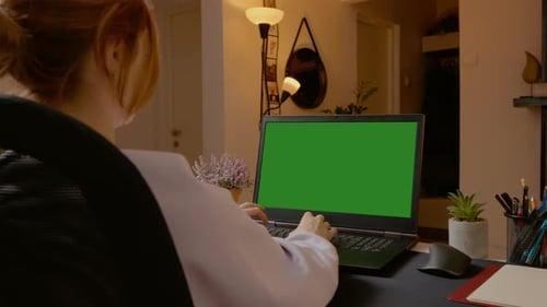Woman working from home typing on a laptop with green screen