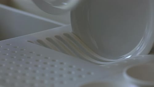Close up shot of a dinner plate being placed in a drying rack after being washed.