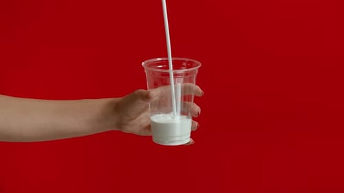 Vista amplia de las manos de una mujer vertiendo leche en un vaso de plástico vacío