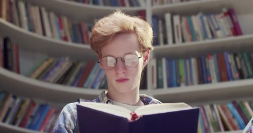 Close Up of Caucasian Redhaired Young Male Student in Glasses Reading Book and Searching for