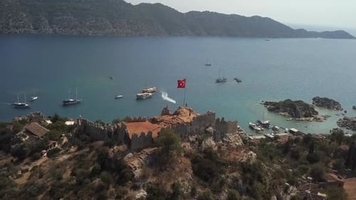 Ruinen der Burg Simena am Meer auf einem felsigen Hügel unter türkischer Flagge, Luftbild
