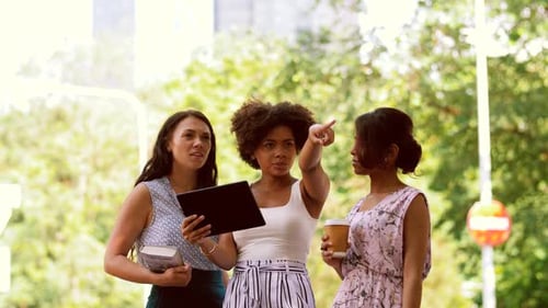 Three women looking at a tablet outdoors