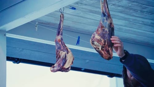 Raw Meat Shanks Hang from Wire Under a Ceiling