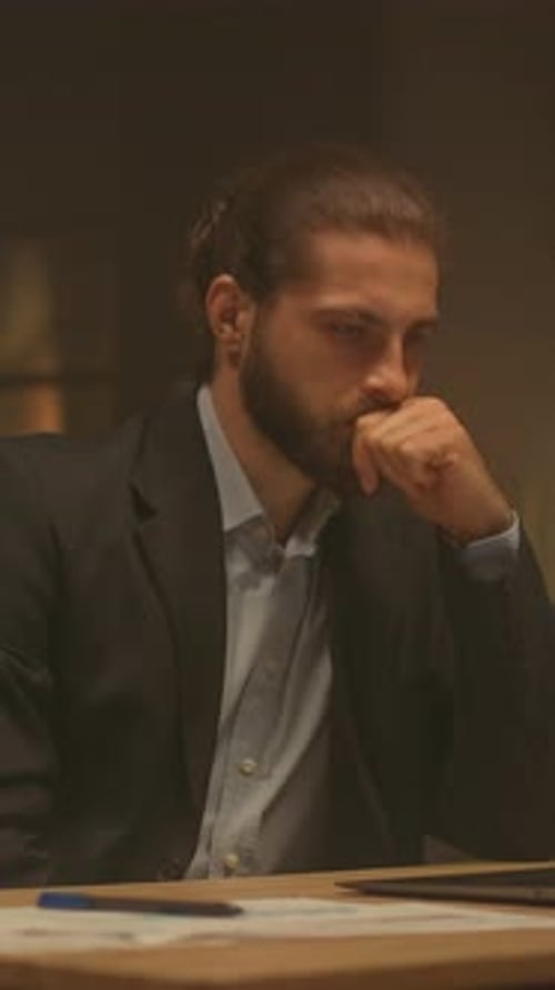 Serious man works late at desk with laptop