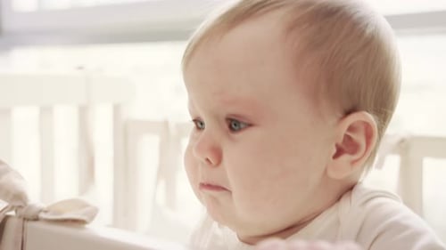 Sad Infant Girl Gnawing Baby Cot. Little Baby Cry in Bed. Crying