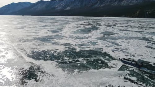 A trip across an icy lake in a hovercraft. Mottled ice at foot of the mountains
