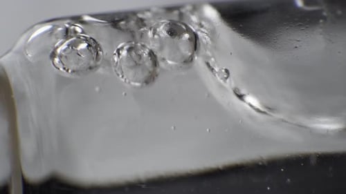 Macro shot of clear liquid with few bubbles on the surface slowly moving in reagent tube.
