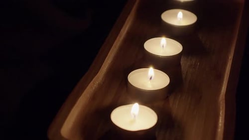 Fond sombre et maussade : des bougies à thé brûlent dans un plateau en bois décoratif