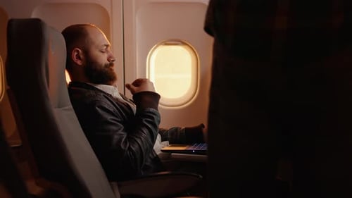 Man Sleeping on Airplane with Passenger Using Laptop