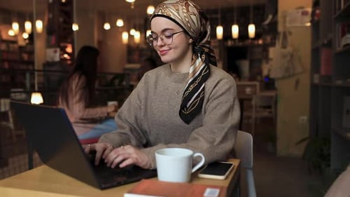 Young woman working at coffee shop while using laptop.