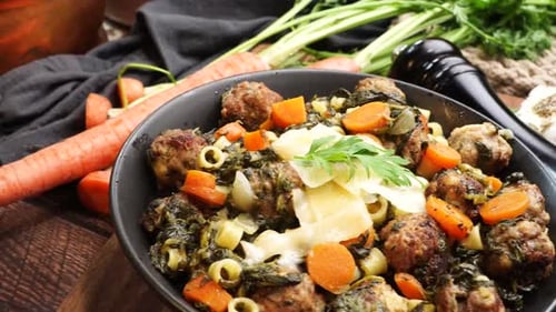 Italian Wedding Soup in a black bowl on a wooden cutting board, close up and panning across the meal