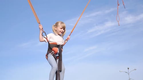 Happy Child Girl Jumping on a Trampoline Against the Blue Sky