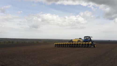 Blue tractor planting sunflower with yellow planter on the field in Ukraine