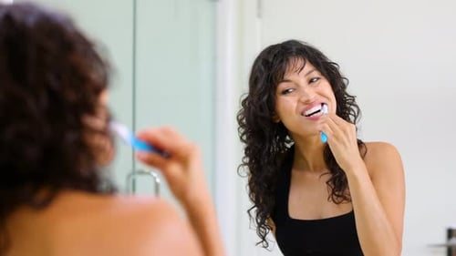 Woman Brushing Teeth in Bathroom Mirror
