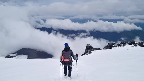 Male Mountaineer with Trekking Poles and a Backpack Walking on Mountain Ridge