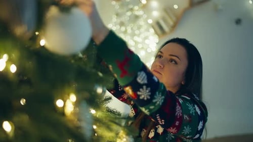 Woman Decorates Christmas Tree with Ornaments at Home